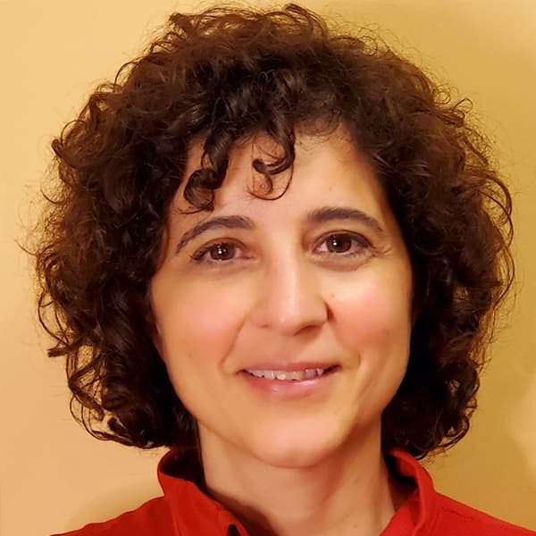 A woman with short curly hair and a red shirt looking at the camera and smiling