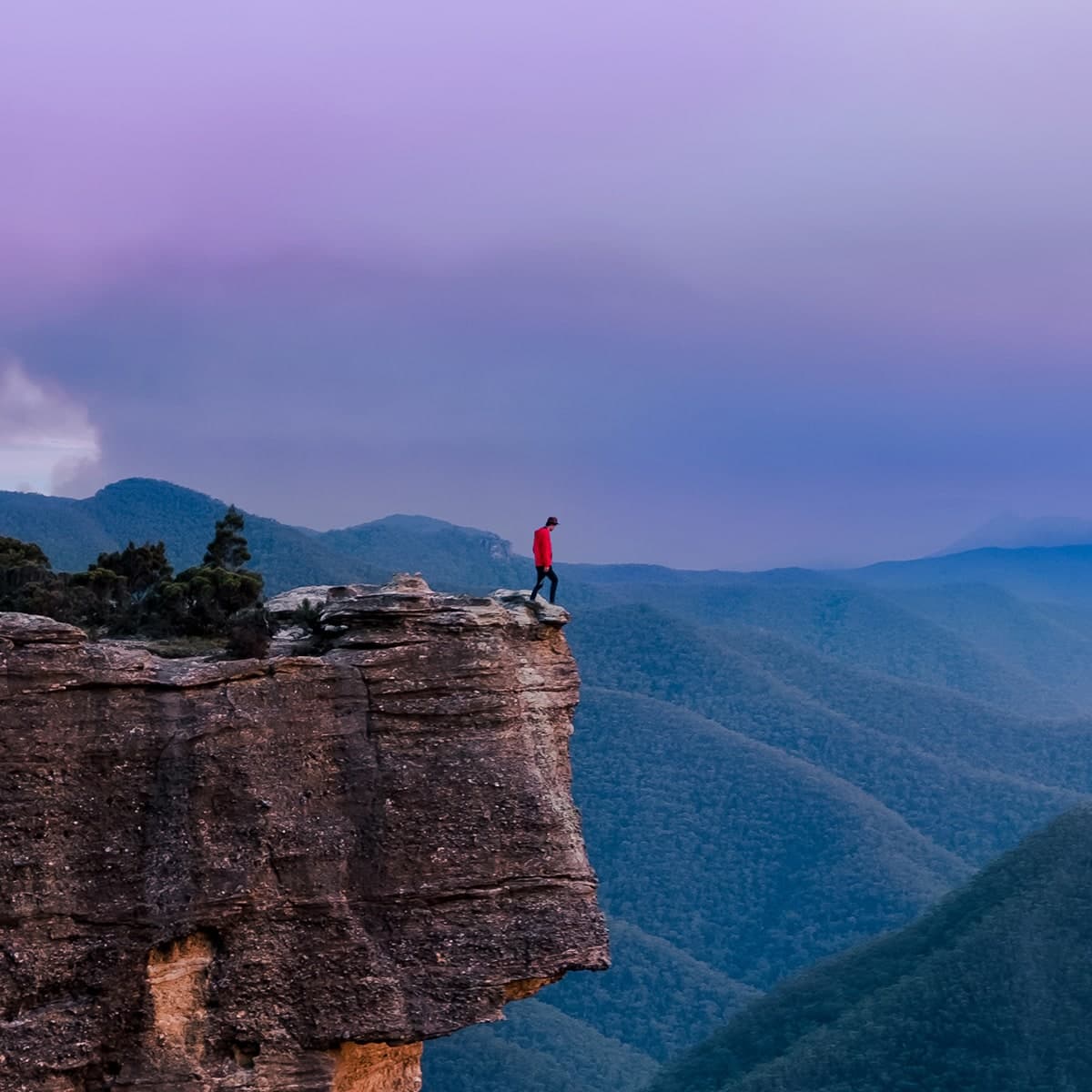 home-siftbox-standing-on-mountain A man wearing a bright red jacket standing on the edge of a cliff at dusk